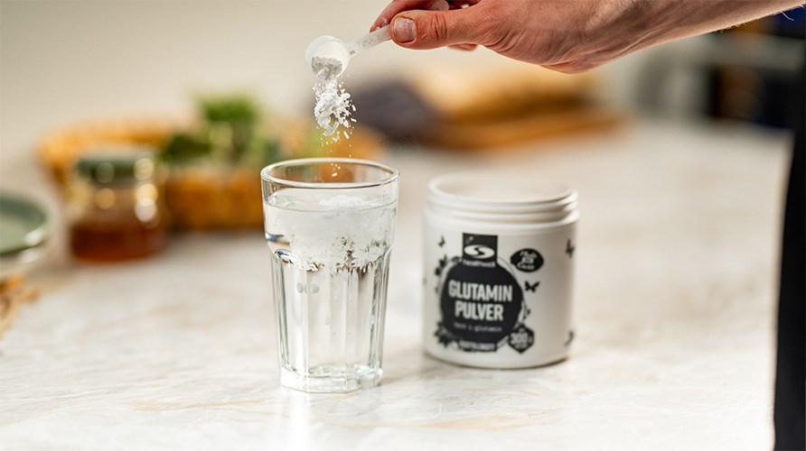 Billede af et glas og en person, der h�lder en skefuld glutaminpulver i glasset.